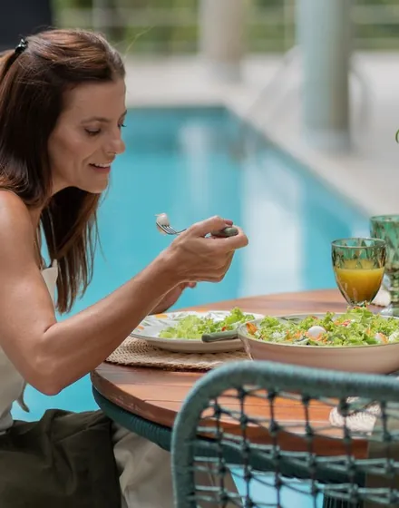 Mulher almoçando uma salada à beira da piscina